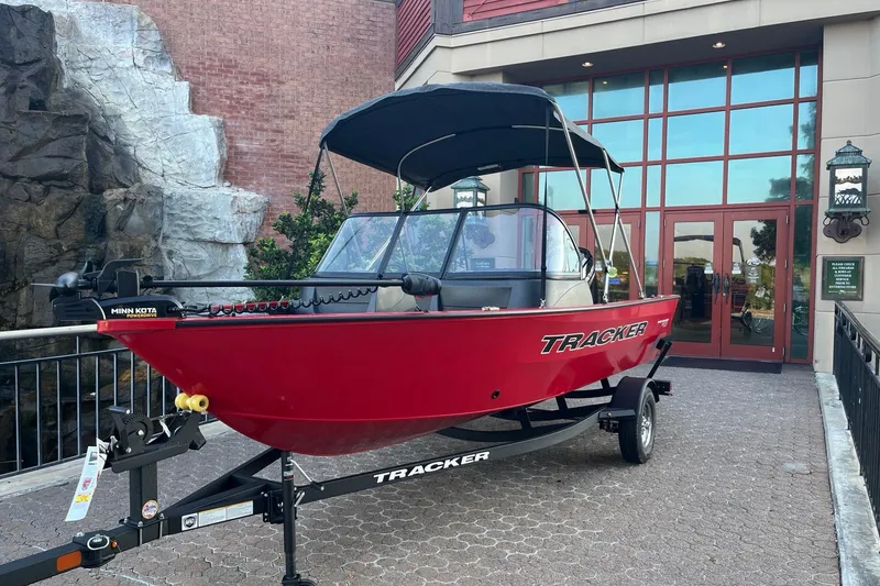 The Image of 2026 Tracker Pro Guide V-16 WT boat displayed outdoors, featuring a red hull and canopy. - 0