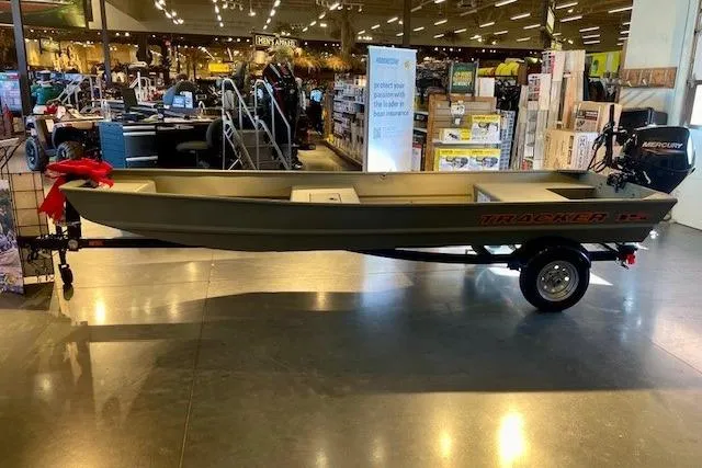 Slide: The Image of 2026 Tracker Grizzly 15 Jon boat displayed in a showroom with a Mercury motor. - 19