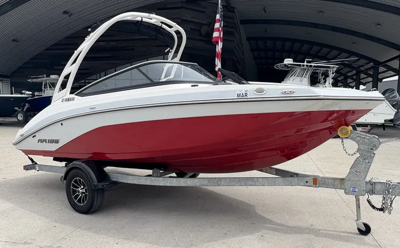Slide: The Image of 2024 Yamaha AR 195 boat with red hull on a trailer, parked outdoors. - 3