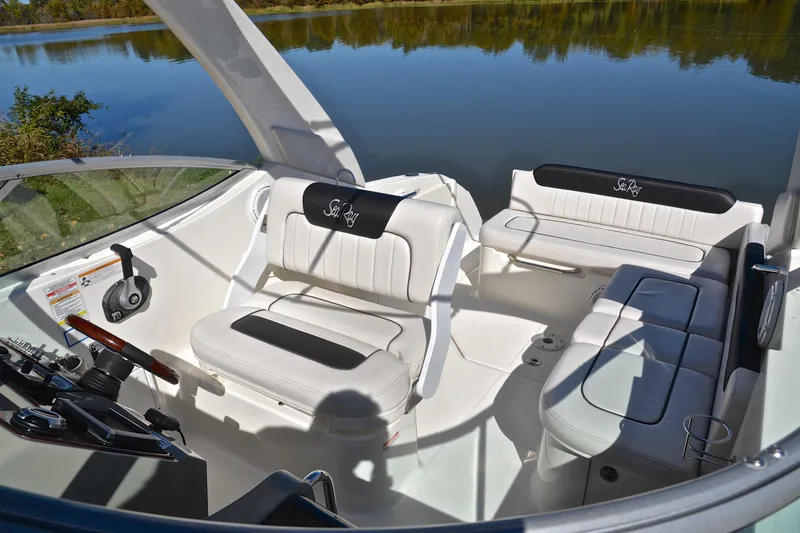 Slide: The Image of 2011 Sea Ray 260 Sundancer boat interior with white seating and steering wheel by a lake. - 24