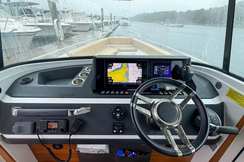 Slide: The Image of 2020 Axopar 28 Cabin helm with navigation screens, steering wheel, and wet bar in rainy marina. - 17