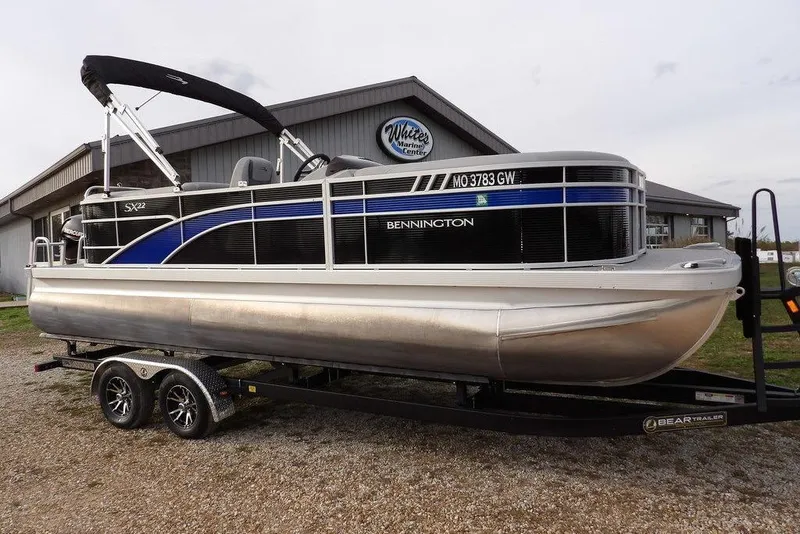 The Image of 2024 Bennington 22 SXS pontoon boat on trailer, parked outside a marine center. - 0
