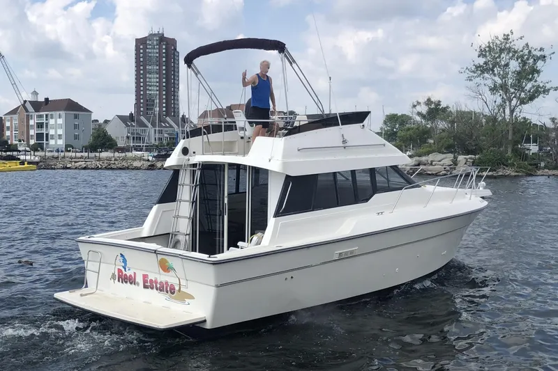 The Image of 1990 Silverton 34 Convertible boat named "Reel Estate" on water near urban shoreline. - 0