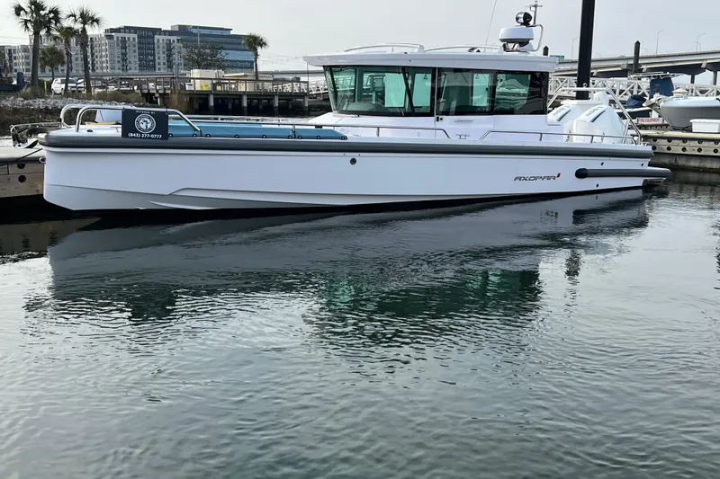 The Image of 2023 Axopar 28 Cabin boat docked at sunset with flags and buildings in the background. - 0