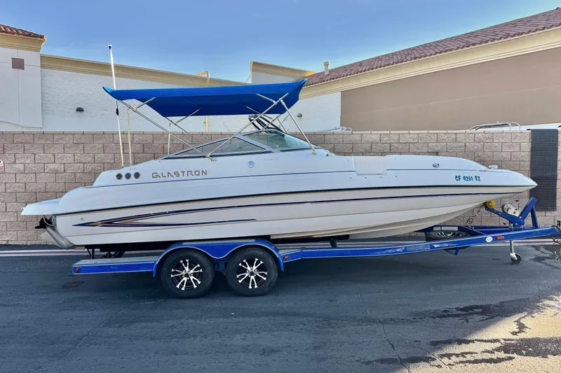 The Image of 2004 Glastron DX 235 Deckboat on trailer with blue canopy, parked outdoors. - 0