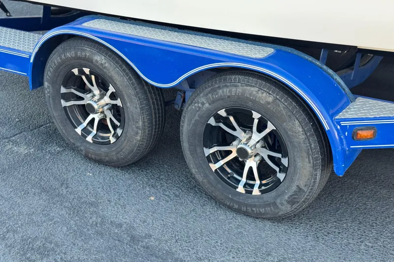 Slide: The Image of 2004 Glastron DX 235 Deckboat trailer with dual black alloy wheels and blue fender. - 29