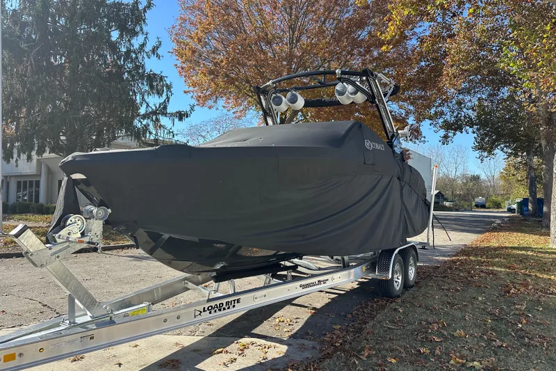Slide: The Image of 2023 Cobalt R6 Surf boat covered on trailer, parked on a leafy street. - 20