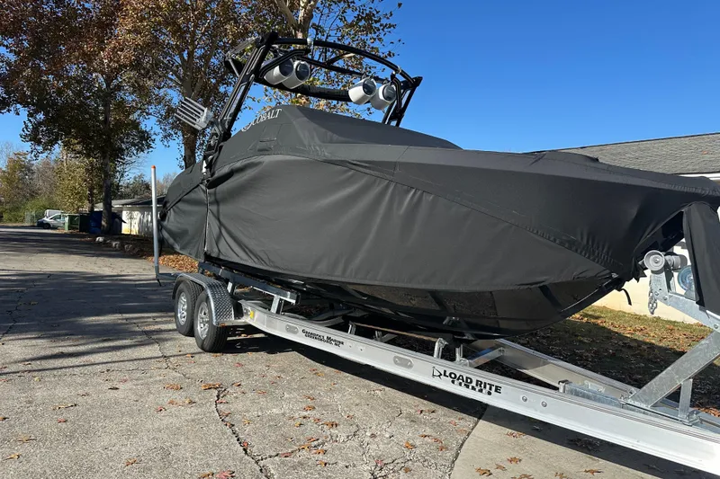 Slide: The Image of 2023 Cobalt R6 Surf boat covered on trailer, parked outdoors under clear blue sky. - 22