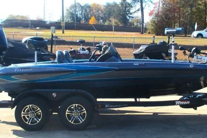 Slide: The Image of 2026 Triton 18 TrX boat on trailer, parked outdoors, with trees in the background. - 8
