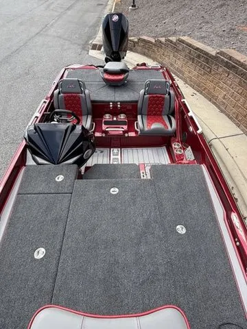 Slide: The Image of 2026 Bass Cat Lynx STS boat with red and gray interior, docked on a paved surface. - 12