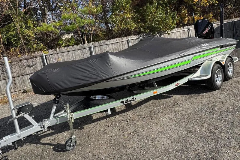 Slide: The Image of 2021 Bass Cat Cougar FTD boat covered on trailer, parked outdoors with trees in background. - 12