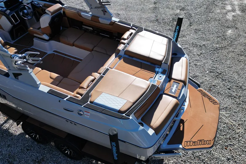 Slide: The Image of 2021 Malibu M220 boat with luxurious seating and sleek design on a gravel surface. - 14