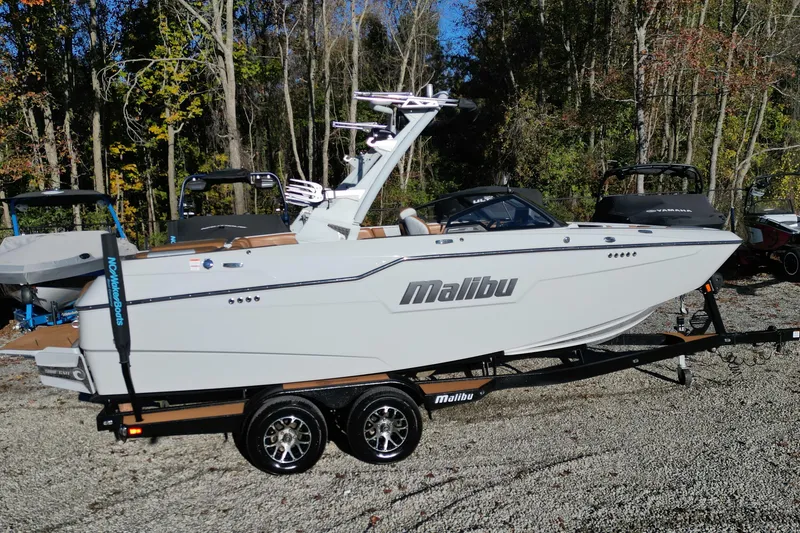Slide: The Image of 2021 Malibu M220 boat on trailer, parked outdoors with trees in background. - 3