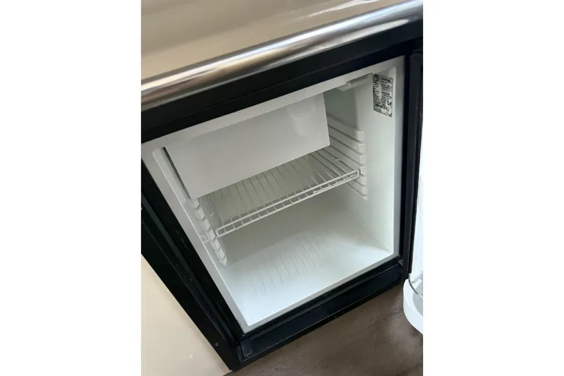 Slide: The Image of Open mini fridge inside 1996 Sea Ray 270 Sundancer boat, showing interior shelves. - 26