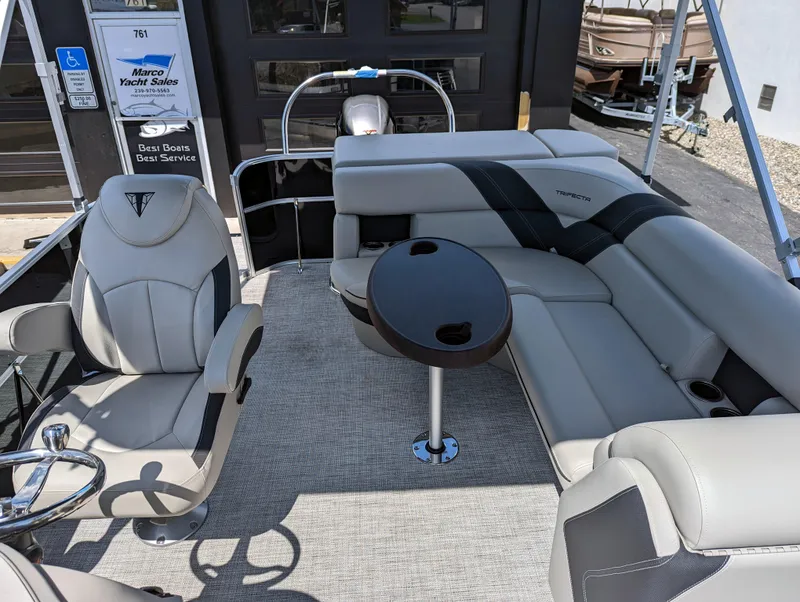 Slide: The Image of 2022 Trifecta 20C LE pontoon boat interior with seating and canopy, parked near a building. - 10
