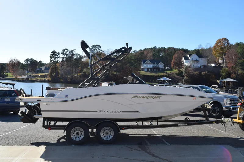 The Image of 2023 Starcraft SVX 210 IO boat on trailer by a scenic lakeside. - 1