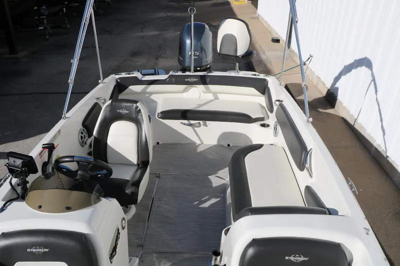 Slide: The Image of 2018 Stingray 182 SC boat interior with seating and steering wheel, docked outdoors. - 23