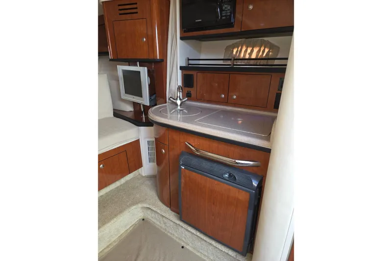 Slide: The Image of 2007 Sea Ray 290 Sundancer interior with kitchenette, featuring wood cabinetry and modern appliances. - 16