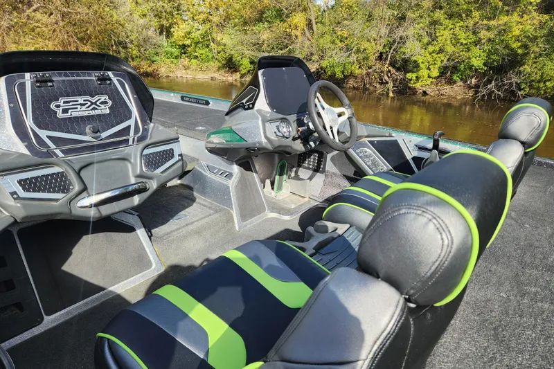 Slide: The Image of 2019 Skeeter FX21 boat interior with green-accented seats and steering wheel, near a riverbank. - 16
