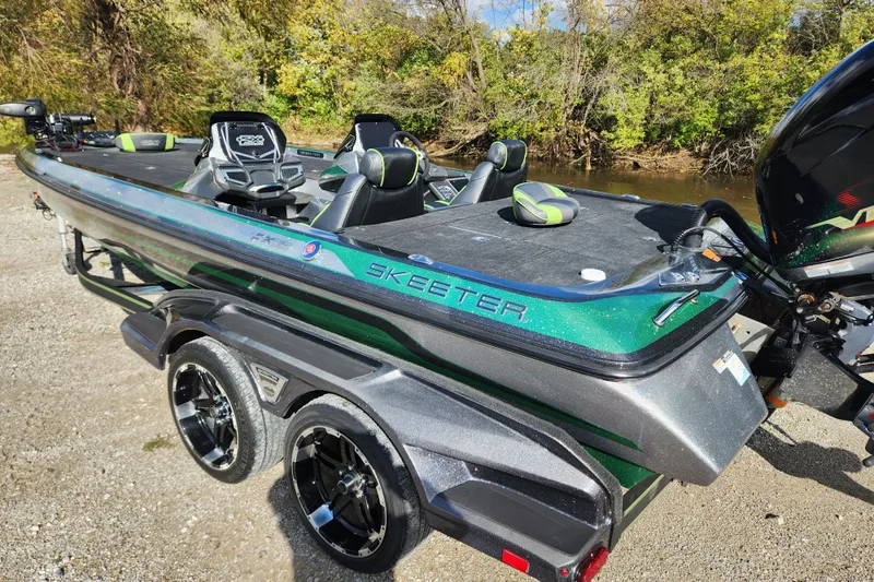 Slide: The Image of 2019 Skeeter FX21 boat on trailer, parked near a riverbank with lush greenery. - 7