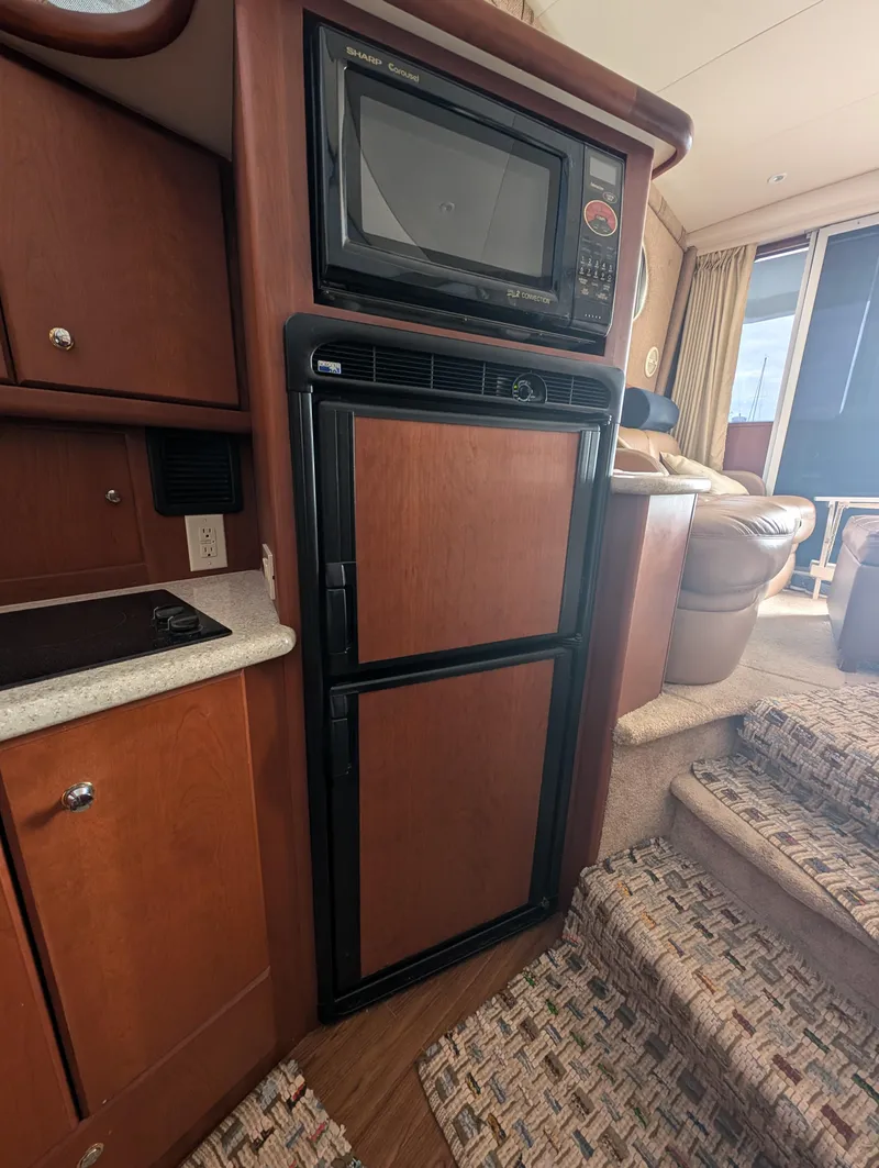 Slide: The Image of 2005 Silverton 34 Convertible interior with microwave and fridge, featuring wood cabinetry and carpeted stairs. - 8