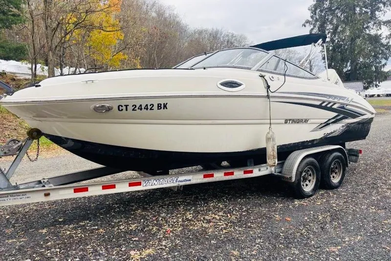 The Image of 2018 Stingray 214 LR boat on trailer, parked outdoors with autumn trees in background. - 0
