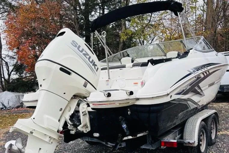 Slide: The Image of 2018 Stingray 214 LR boat with Suzuki outboard motor on trailer, surrounded by autumn trees. - 2