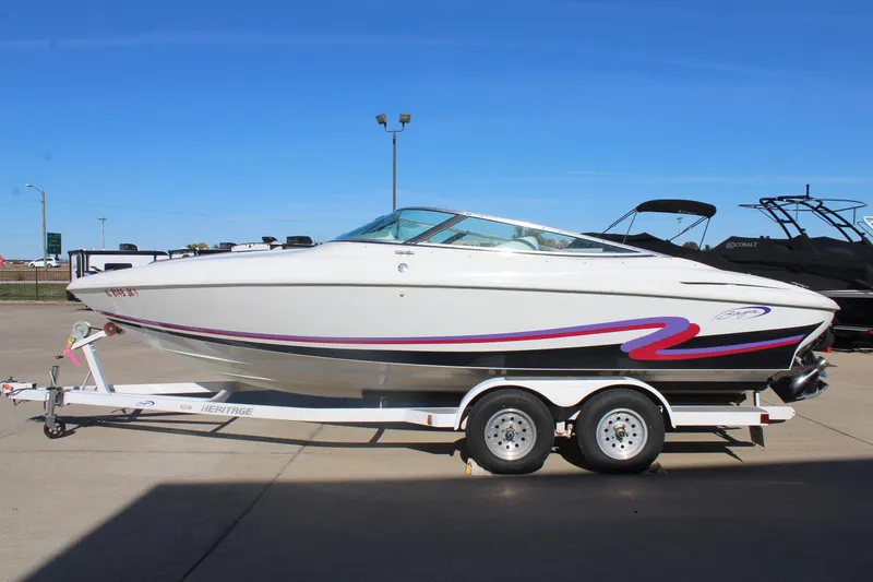 Slide: The Image of 1996 Baja 232 speedboat on trailer, white with red and purple accents, parked outdoors. - 5