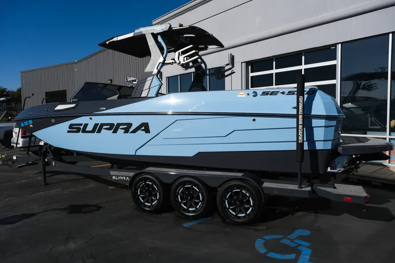 Slide: The Image of 2025 Supra SE550 boat in light blue on a trailer, parked outside a building. - 3