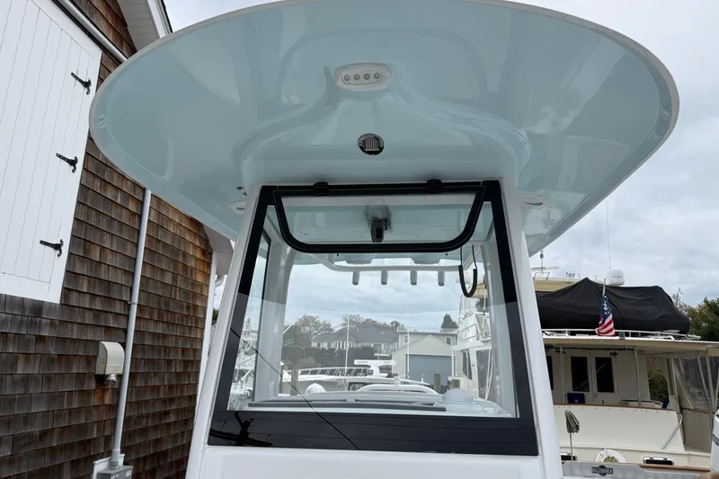 Slide: The Image of 2026 Sea Hunt Ultra 235 SE boat with T-top and windshield, docked near wooden building. - 8