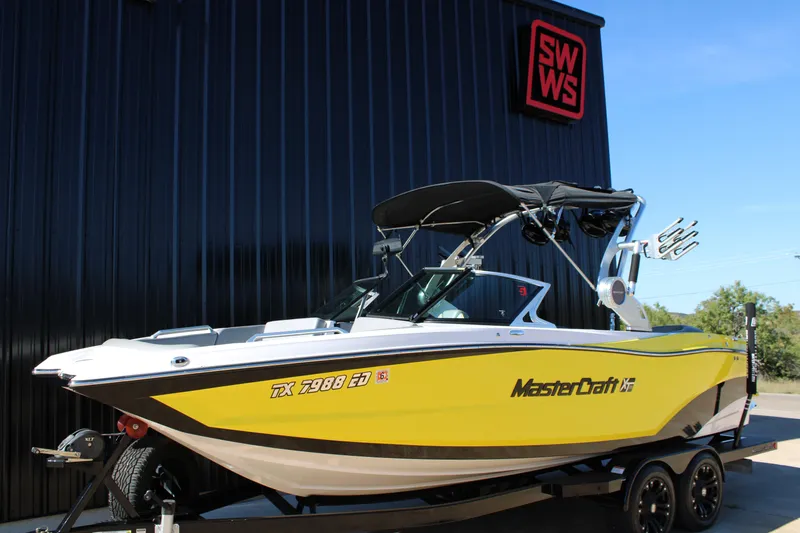 The Image of 2018 MasterCraft XT22 boat in vibrant yellow, parked on a trailer outside a building. - 1