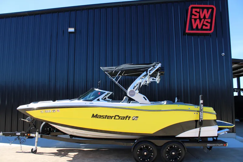 Slide: The Image of 2018 MasterCraft XT22 boat in yellow, parked on a trailer outside a black building. - 2