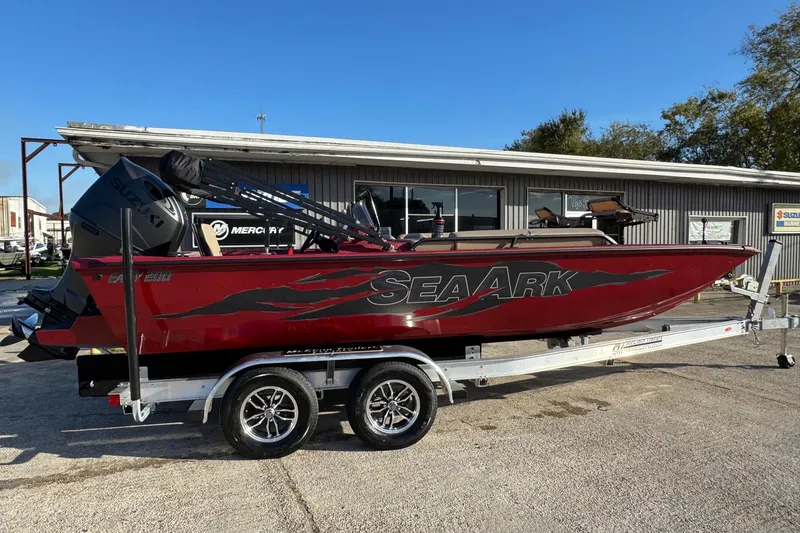 Slide: The Image of 2026 SeaArk Easy 200 boat on trailer, red with black graphics, parked outside a marine shop. - 2