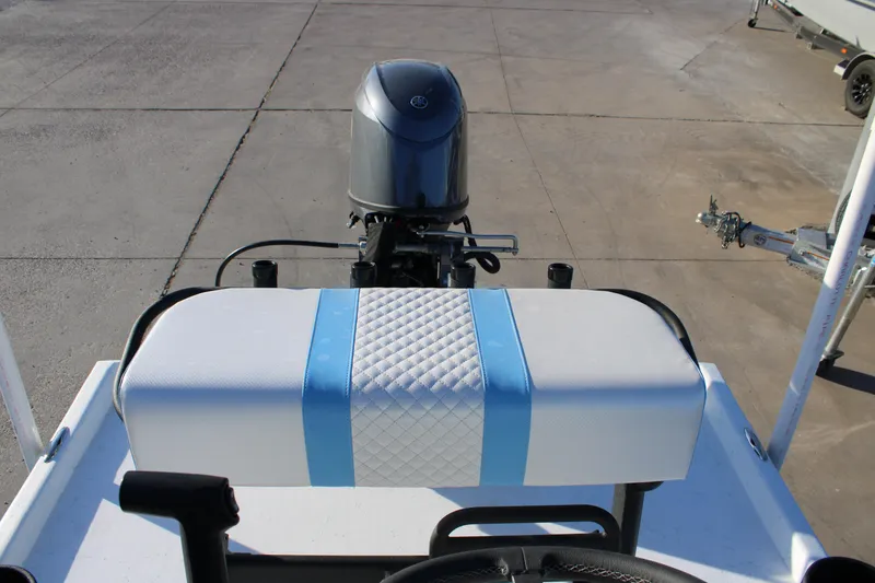 Slide: The Image of 2026 Freedom Boats Chiquita with blue-striped seat and motor, parked on concrete. - 12