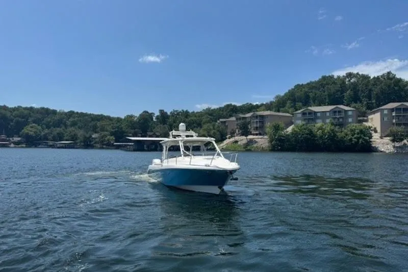 Slide: The Image of 2016 Everglades 360LXC boat cruising on a scenic lake with waterfront homes. - 12