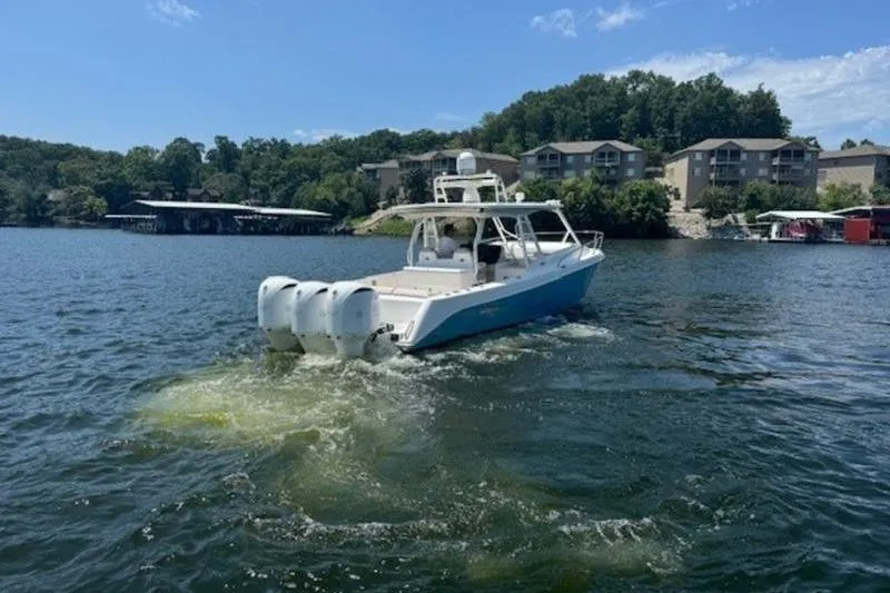 Slide: The Image of 2016 Everglades 360LXC boat cruising on a scenic lake with buildings in the background. - 21