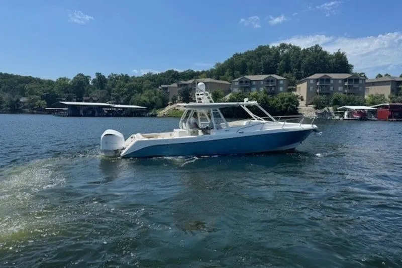 Slide: The Image of 2016 Everglades 360LXC boat cruising on a scenic lake with buildings in the background. - 22