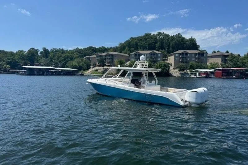 Slide: The Image of 2016 Everglades 360LXC boat cruising on a scenic lake with buildings in the background. - 27