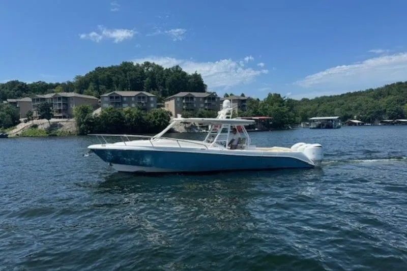 Slide: The Image of 2016 Everglades 360LXC boat cruising on a scenic lake with buildings in the background. - 32