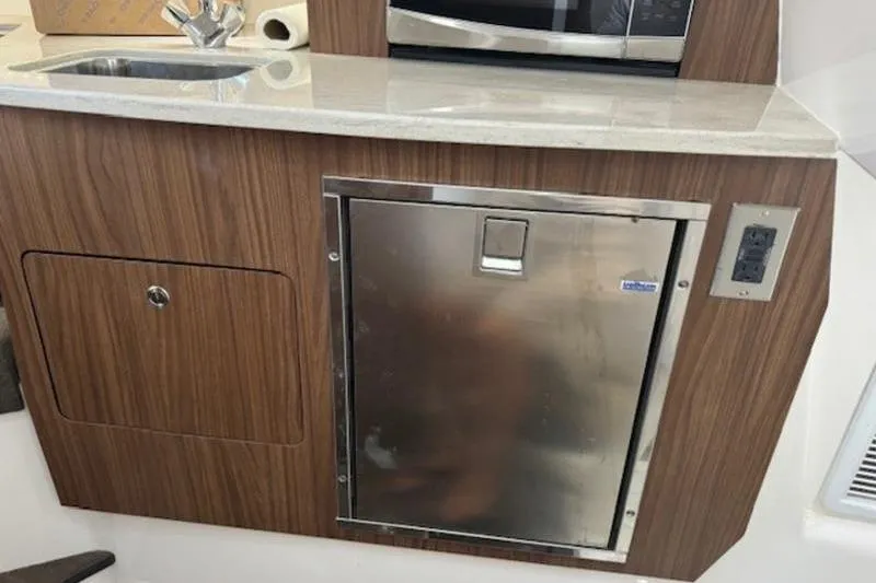 Slide: The Image of 2016 Everglades 360LXC boat interior with kitchenette, featuring sink and stainless steel fridge. - 48