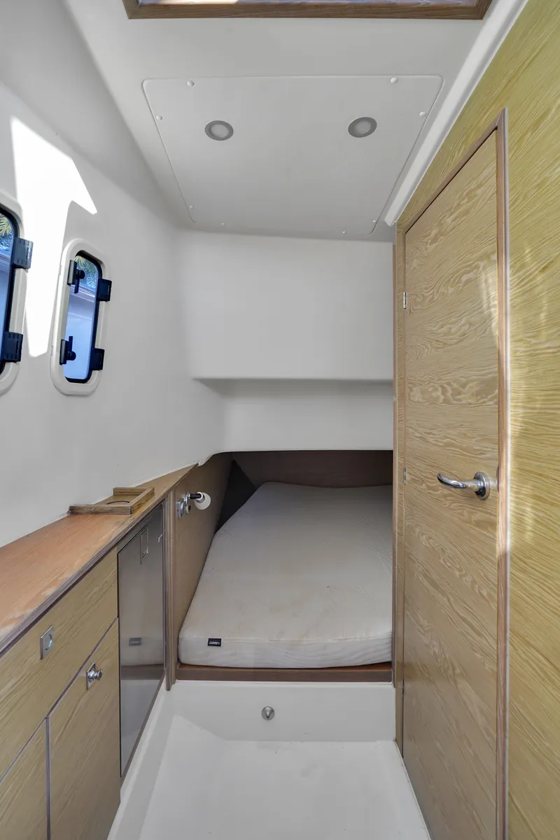 Slide: The Image of 2019 Fjord 38 cabin interior with bed, wooden cabinetry, and porthole windows. - 6