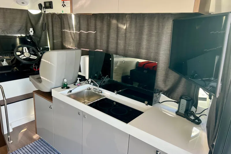 Slide: The Image of 2024 Beneteau Antares 11 interior with helm, kitchenette, and TV setup. - 23