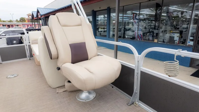 Slide: The Image of 2019 Sun Tracker 24 Party Barge with beige captain's chair, docked near a showroom. - 11
