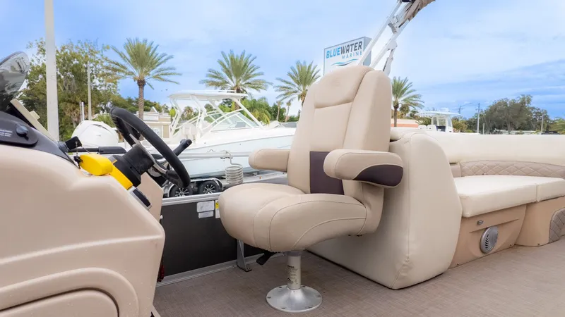 Slide: The Image of 2019 Sun Tracker 24 Party Barge interior with beige seating and steering wheel, docked at Bluewater Marine. - 16