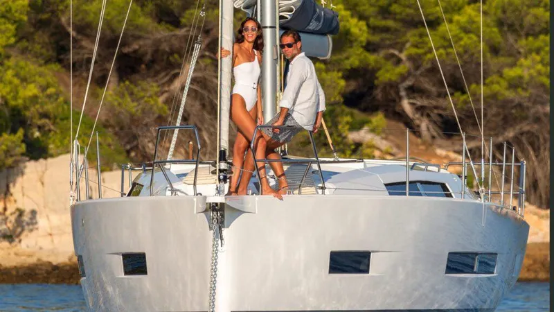 Slide: The Image of 2025 Hanse 410 yacht with two people on deck, sailing near a forested coastline. - 16