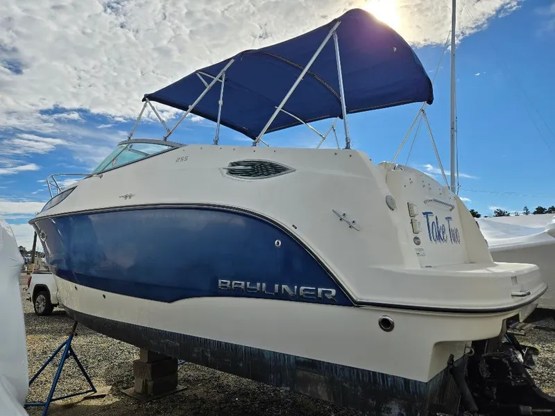 Slide: The Image of 2011 Bayliner 255 boat with blue canopy, docked on land under a partly cloudy sky. - 2