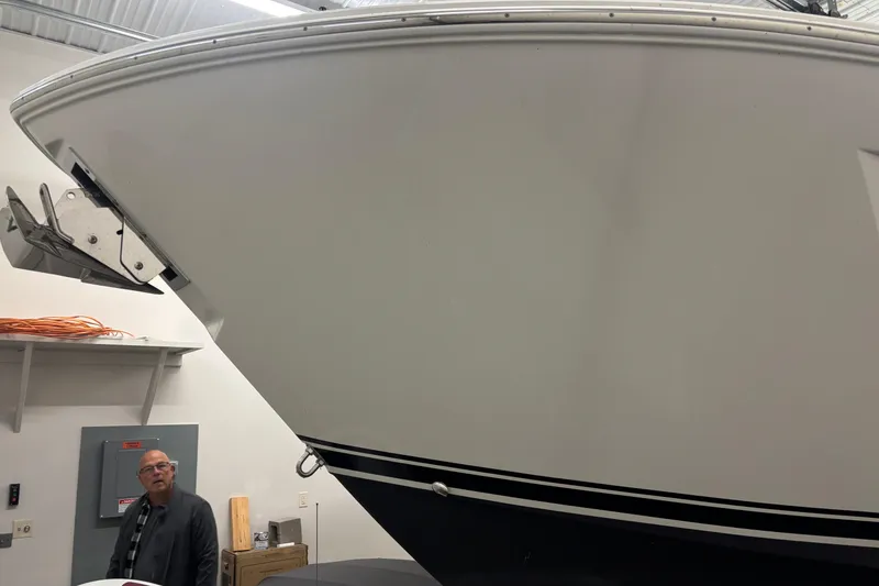 Slide: The Image of 2020 Pursuit DC 365 Dual Console boat in indoor storage, with visible anchor and man nearby. - 60