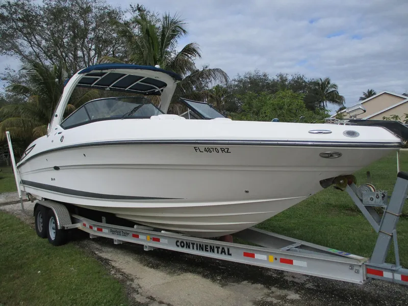 The Image of 2010 Sea Ray 300 SLX boat on trailer, parked outdoors with trees in background. - 0