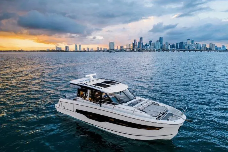 The Image of 2026 Jeanneau NC 1295 Coupe yacht cruising near city skyline at sunset. - 1