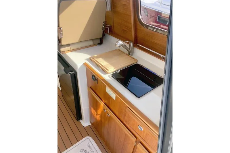 Slide: The Image of 2021 Ranger Tugs R-25 galley with wooden cabinetry, sink, and compact appliances. - 19